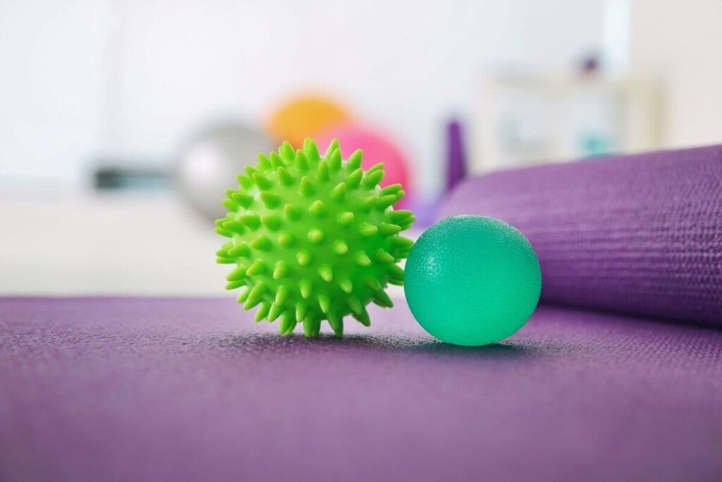 a close up image of two green stress balls laying on a purple matt with some bigger balls laying behind them for children to use in a calm corner for emotional regulation and relaxation