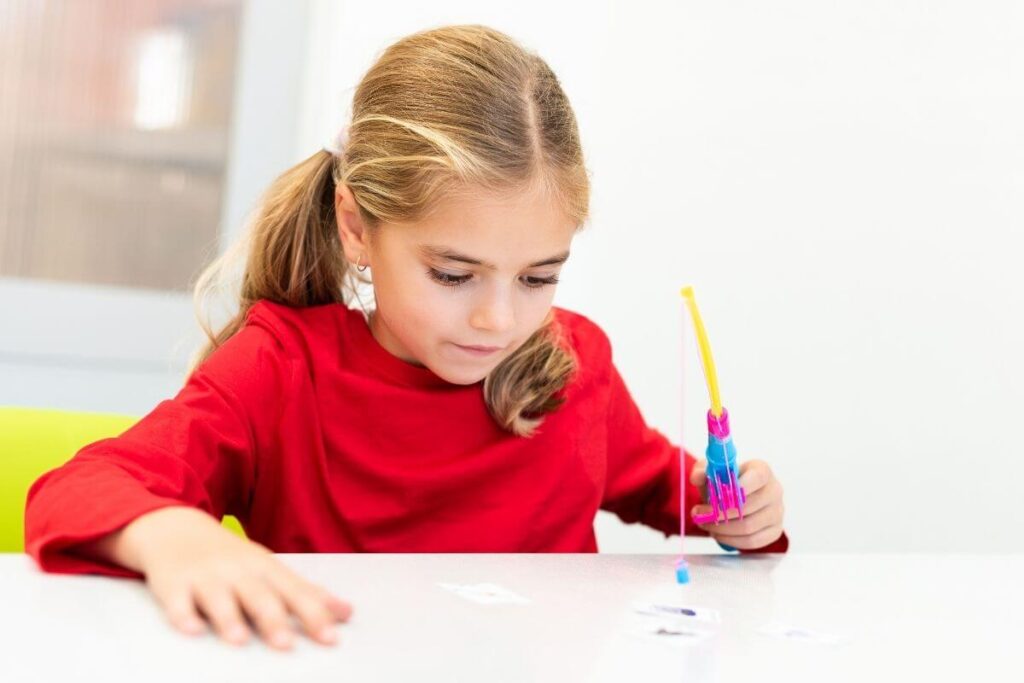 a young girl fidgets with a sensory activity at a table in a calm corner where she is relaxing and getting her emotions under control