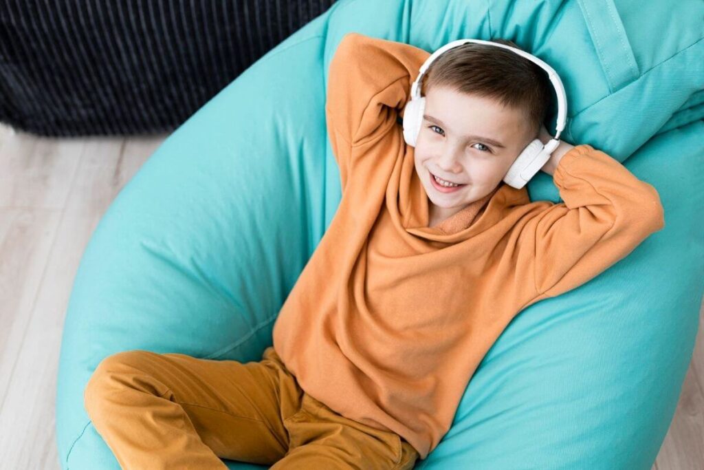 a young boy lays on a turquoise bean bag chair with head phones on listening to an audio book as he calms down in a calm corner