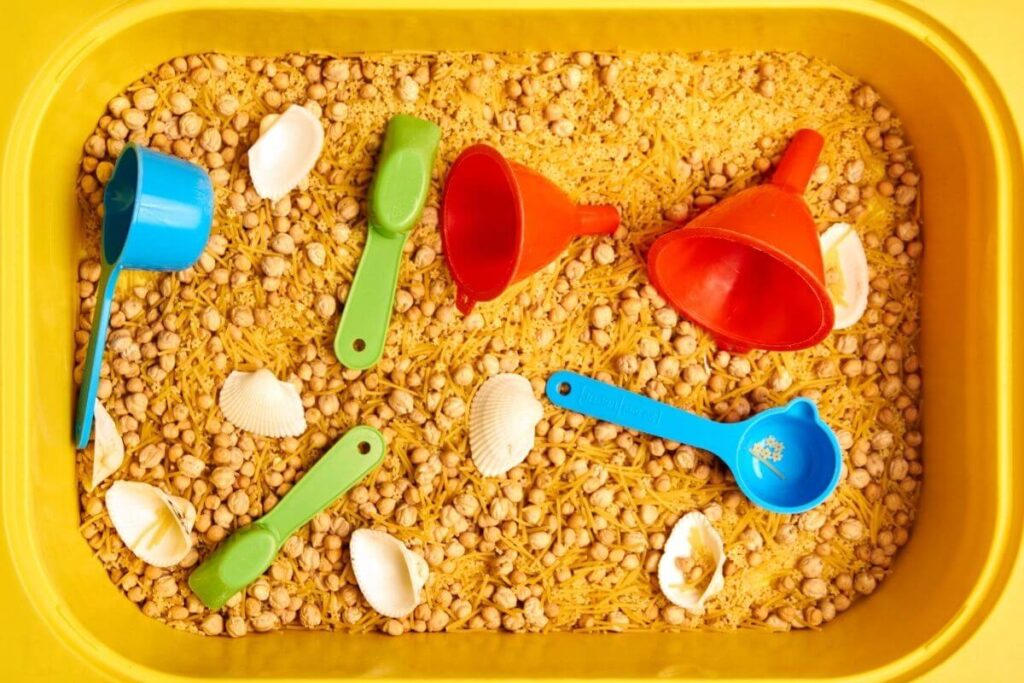 sensory objects including funnels shells teaspoons cups seeds and rice in a bright yellow tray for children to enjoy when they visit the calm corner of their classroom to get their behavior under control