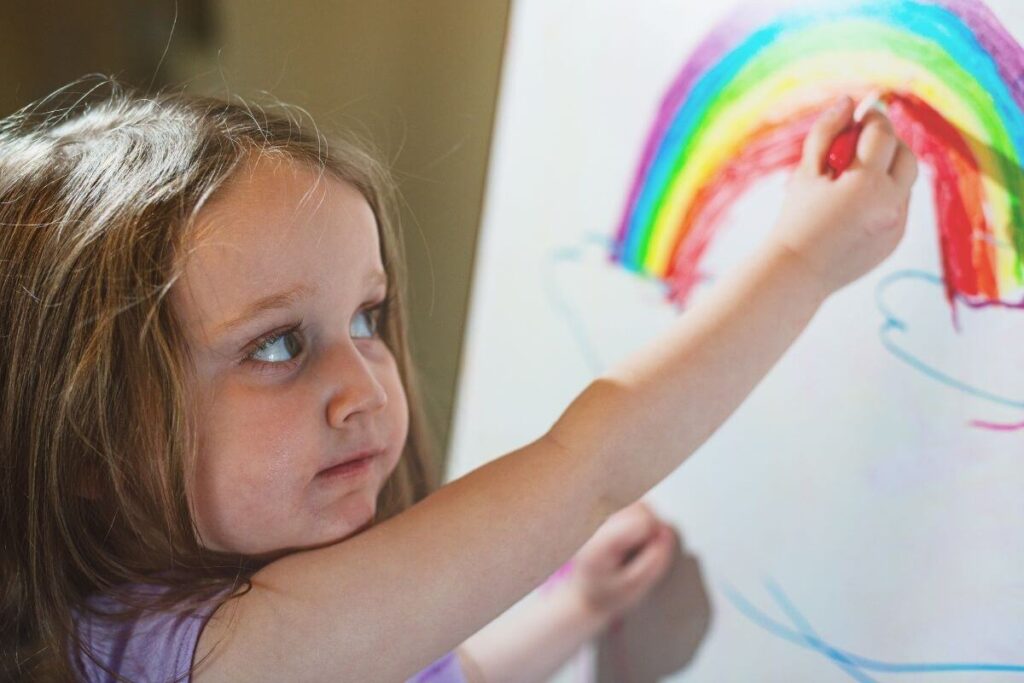 a young girl draws a rainbow on a white board easel as she calms down in a calm corner of her classroom