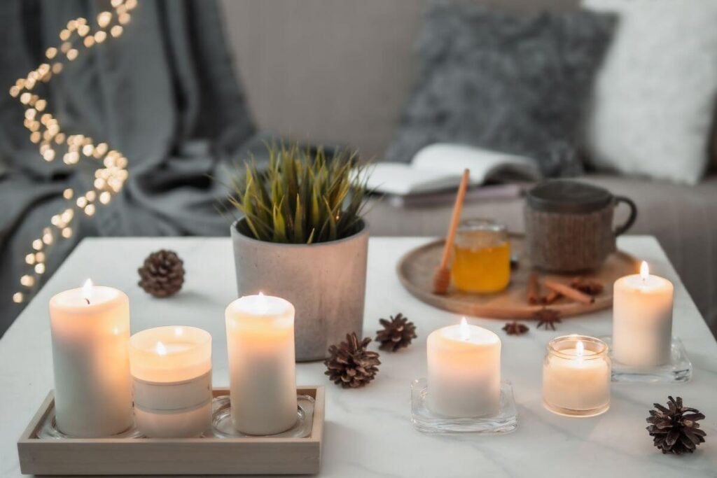 a cozy emotional escape space with candles a plant fairy lights a book a journal pillows a blanket a cup of tea and honey all done in soft neutral tones