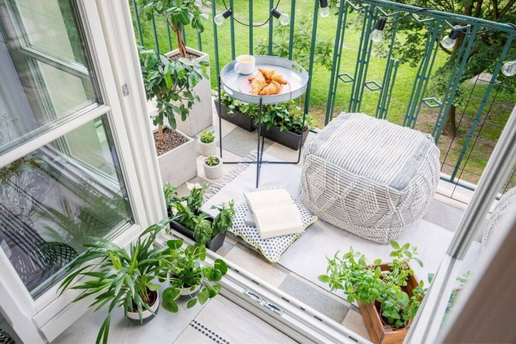 an emotional escape space outside on a balcony with a small table for food and drinks a comfy soft ottoman a book and pillow lots of plants