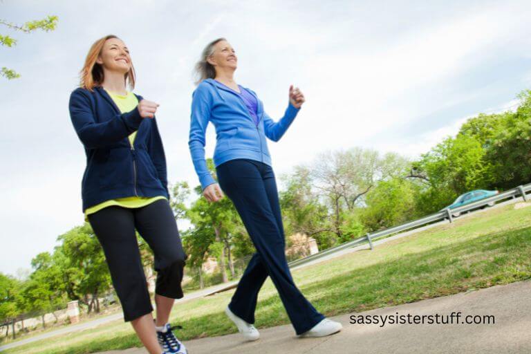 two middle-aged women briskly walk through a park because they know the many benefits of walking for seniors and older adults.