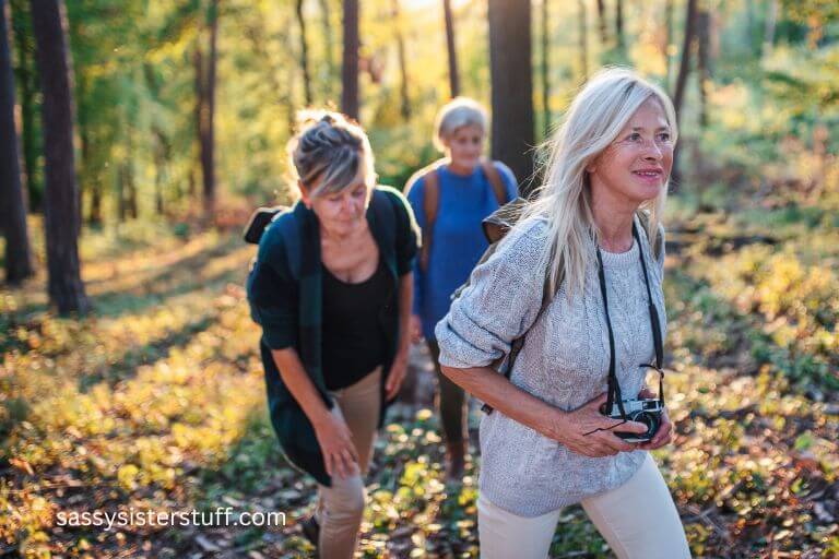 three older women hike through the woods together in the fall.