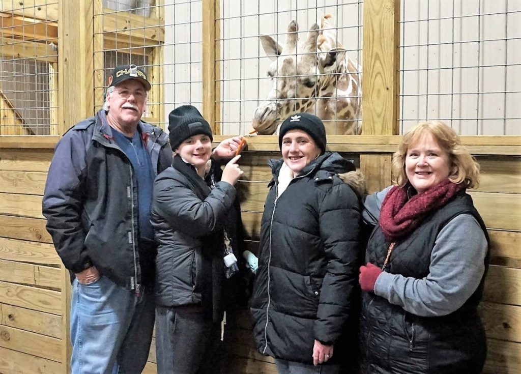 family of four feed carrots to baby giraffe during a holiday visit