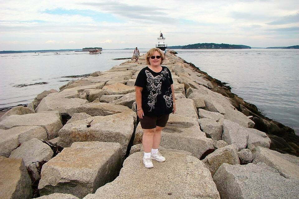 woman standing on boulder walkway in water to get to lighthouse