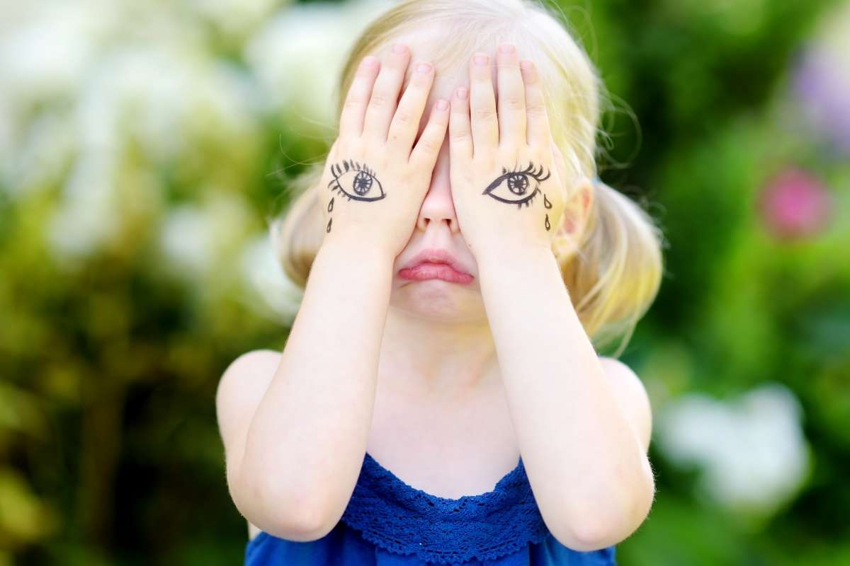 little girl with hands over her eyes pouting and tears drawn on her hands like she is having a mental health breakdown