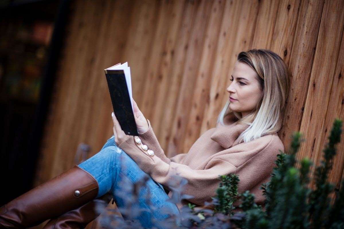 woman leaning against a fence reading a book in the grass