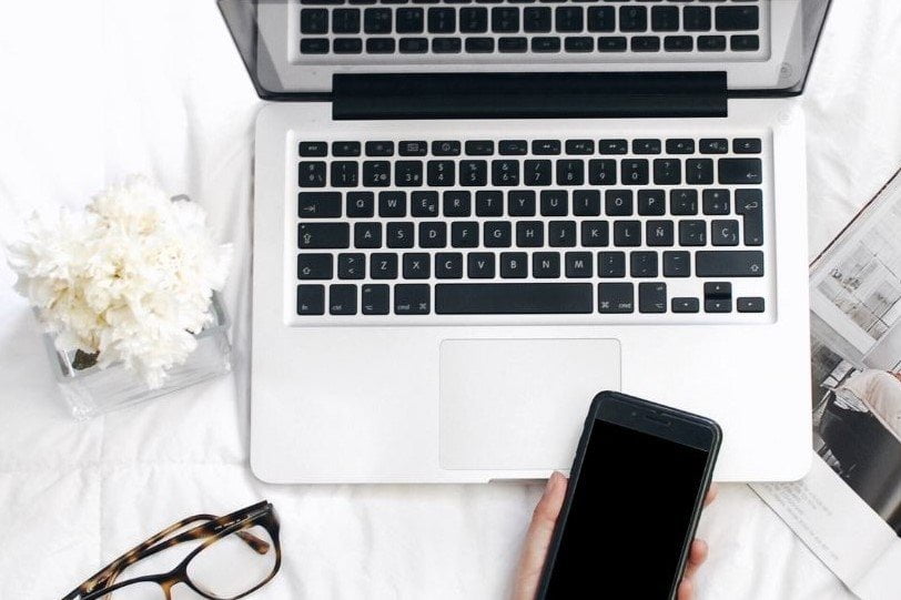 white laptop and flowers eyeglasses and someone holding a phone