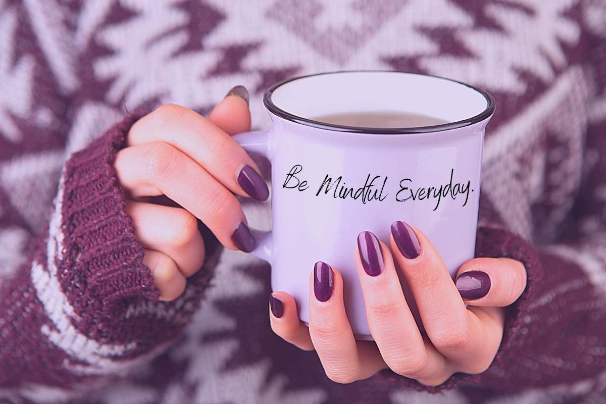 a women with purple nails wearing a cozy purple and white sweater holding a mug that says be mindful everyday