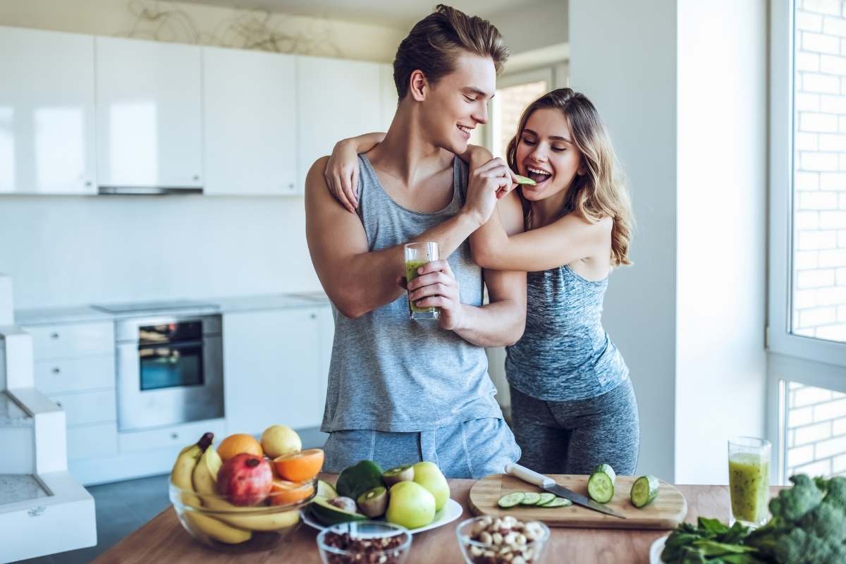 a man and woman in a kitchen cutting fruits and vegetables together