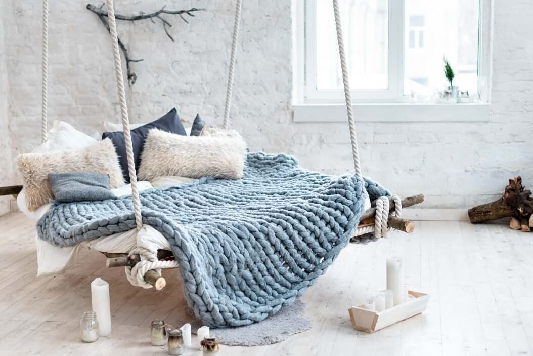 a large multi person hammock with a blue afghan blue pillows white pillows candles sitting on the floor and natural wood decor around it