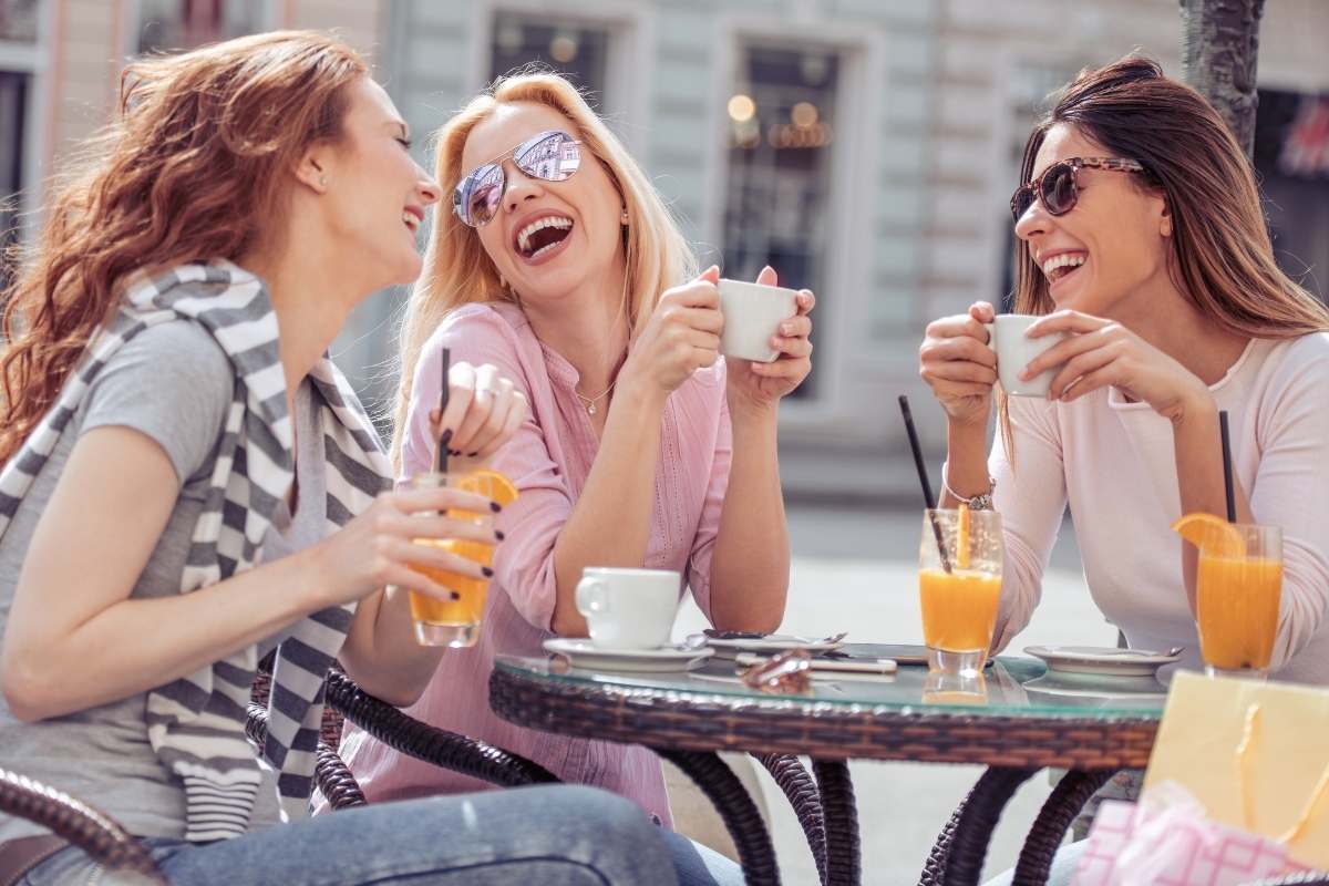 3 female friends sit at an outdoor cafe laughing together