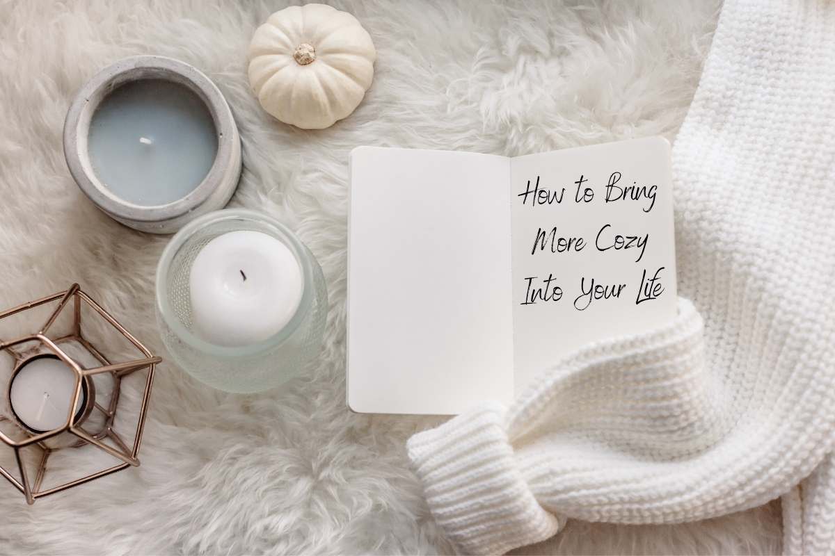 a white flatlay with a small pumpkin 3 candles a small notebook a sweater on a fur blanket