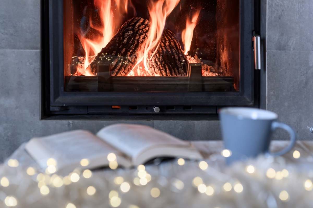 fairy lights a mug and a book laying on a table in front of a fire place