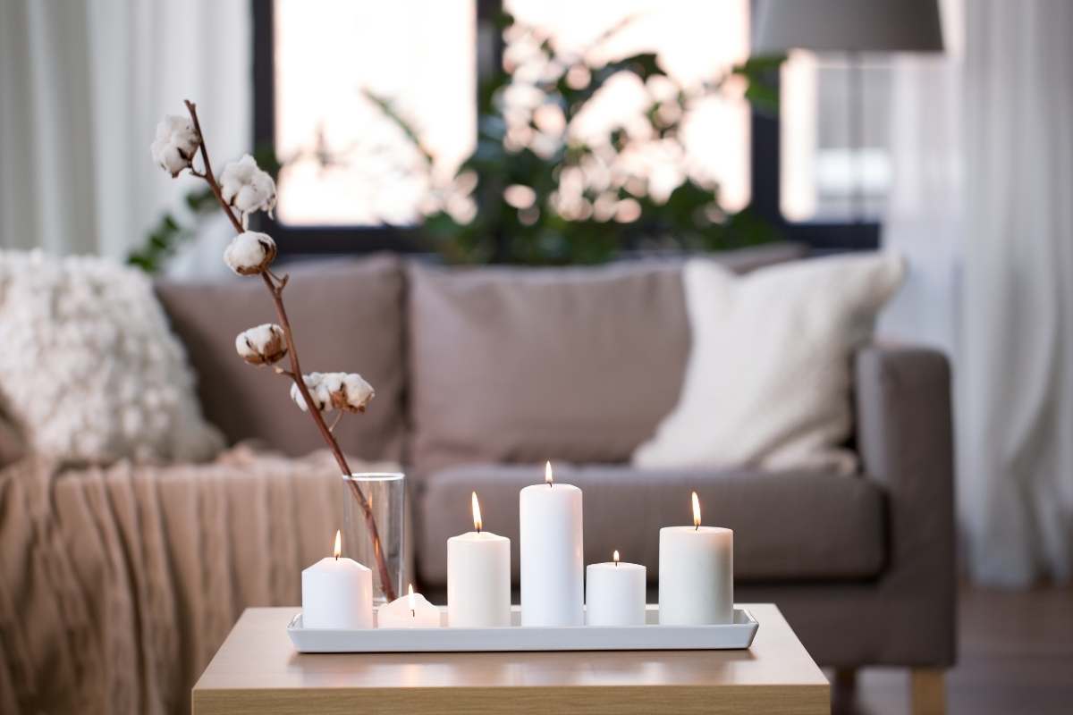 candles burning on a small table in front of a cozy sofa with pillows and a blanket all in neutral cream and white colors