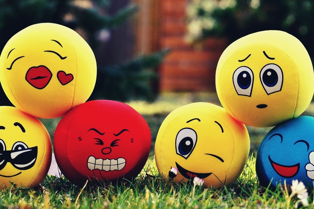 six emoji balls yellow blue and red laying in the grass to help improve happiness