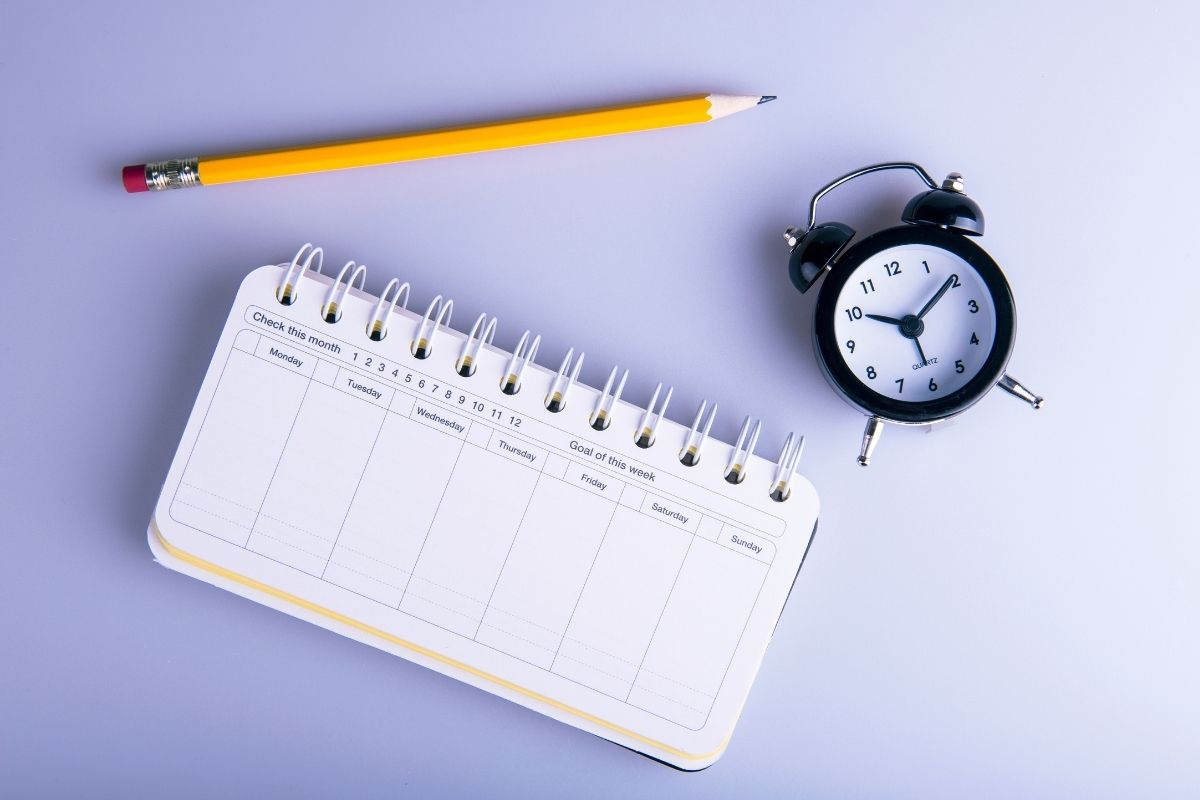 spiral notebook pencil and clock in an image to represent intentional ways to improve your happiness