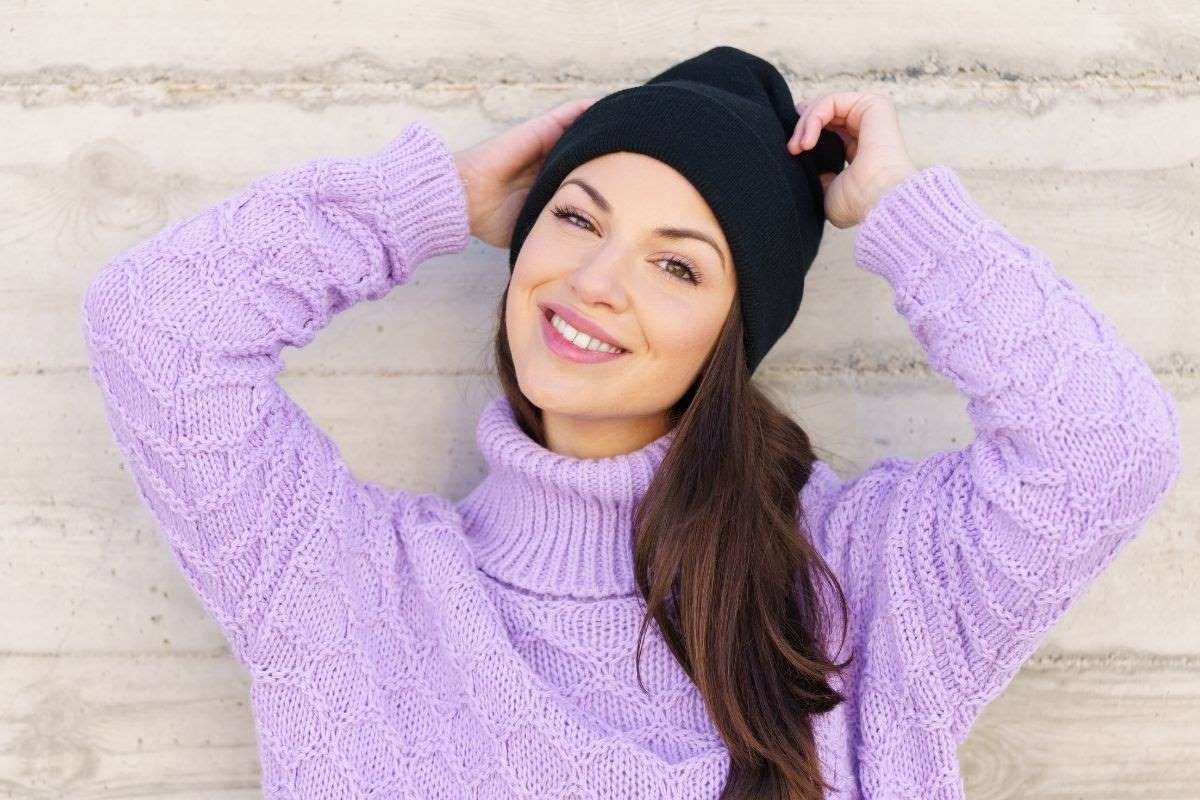 women in a lavender sweater and black hat smiling very happy