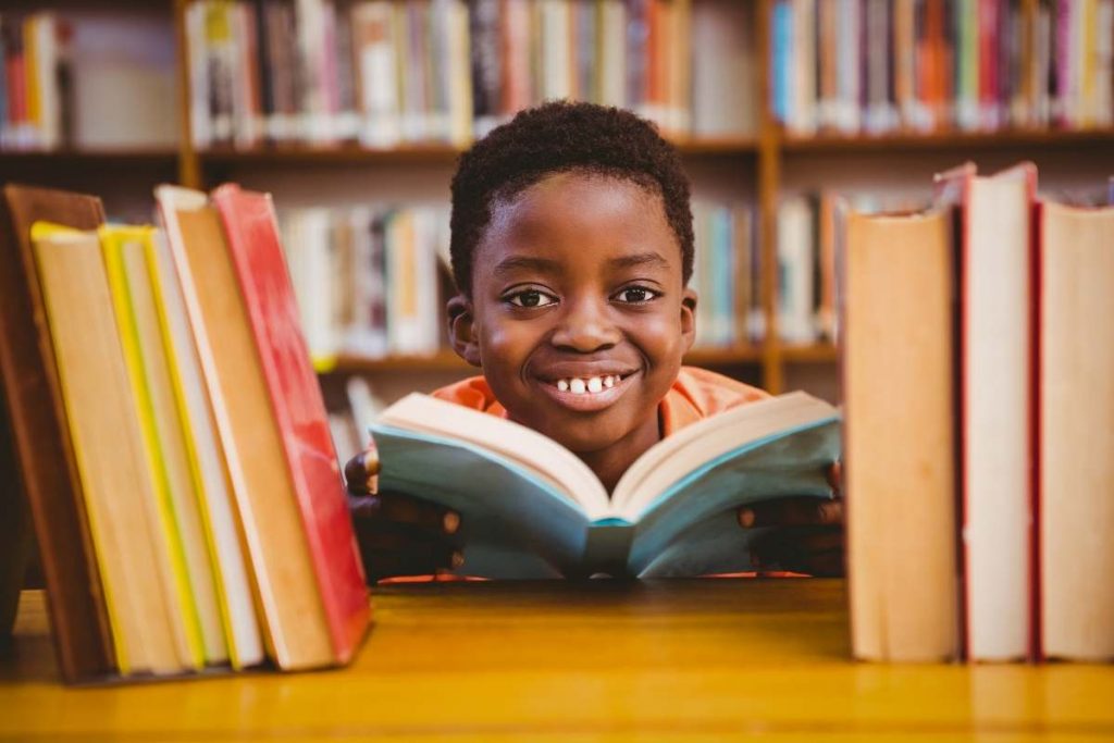 student with a big smile on his face surrounded by books