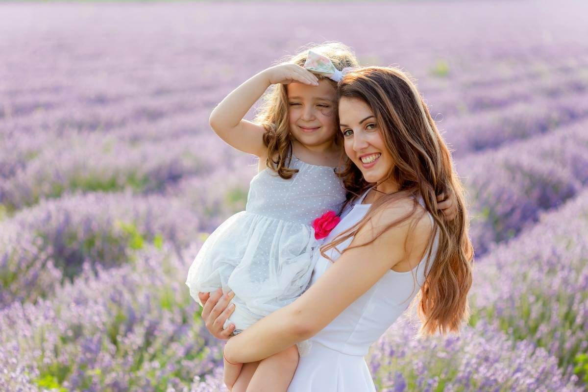 older sister holding a younger sister standing in a field of lavender flowers