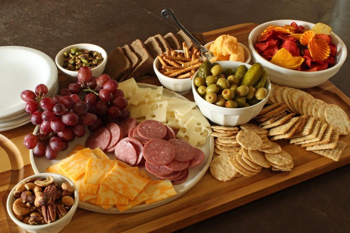 rectangular wooden charcuterie board with dishes of snacks