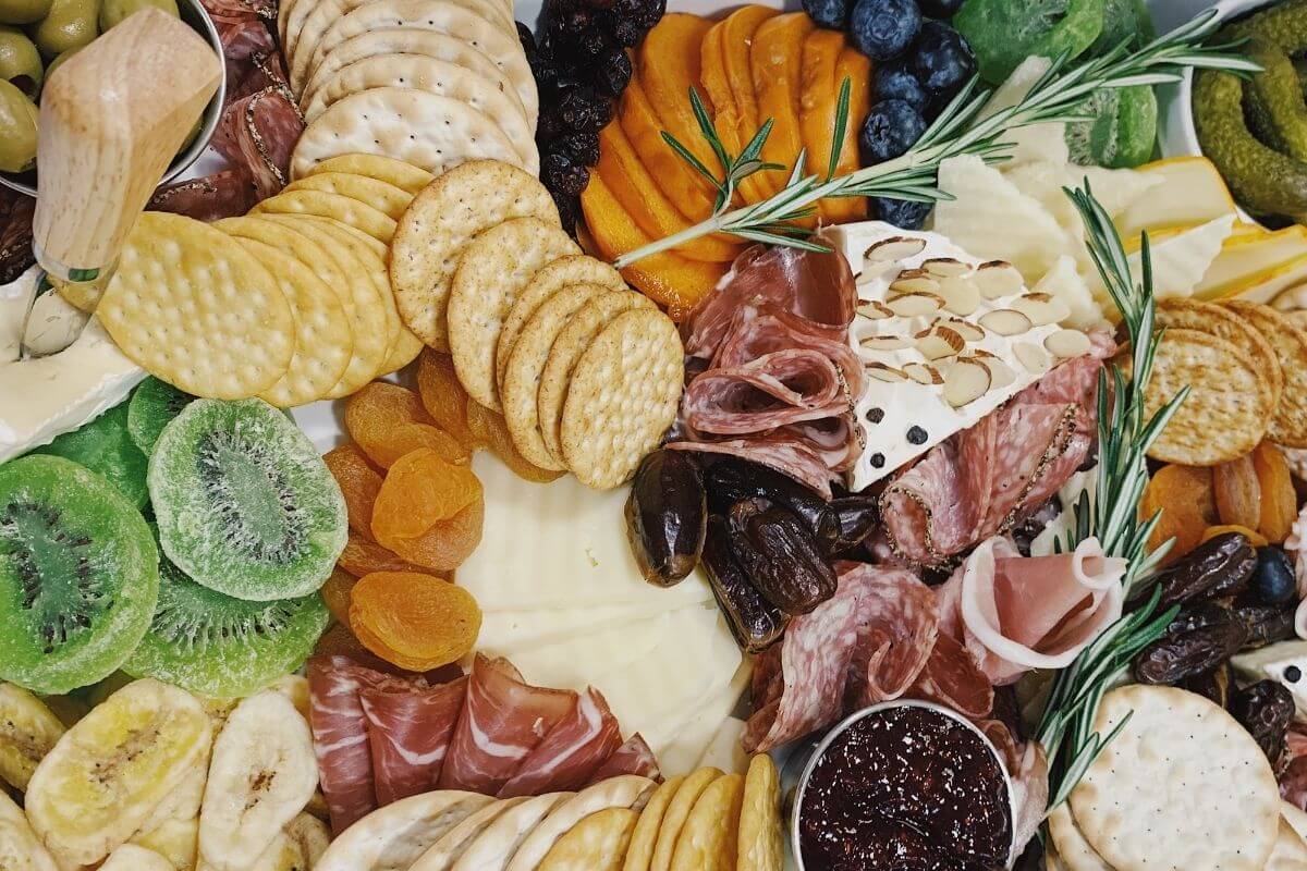 close up of charcuterie board with crackers meats cheese pickles kiwi banana jelly figs and rosemary garnish