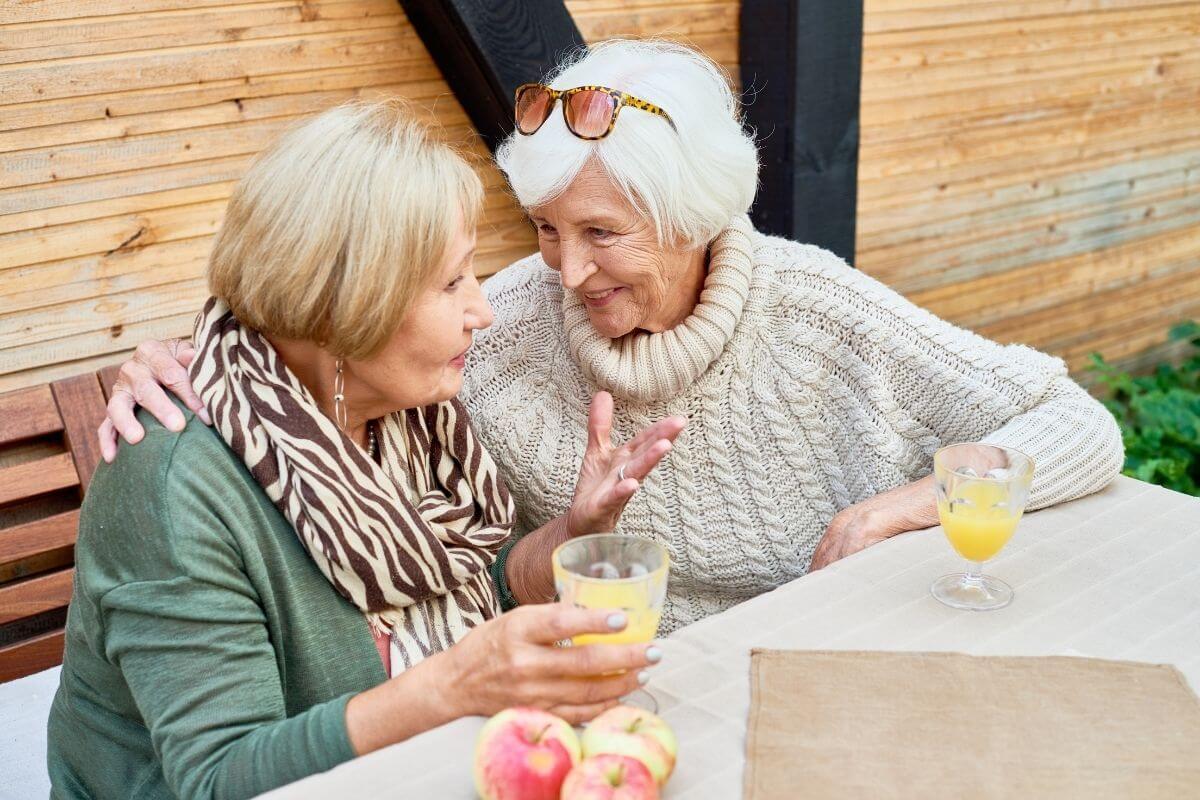 two happy older ladies sit together at a table socializing