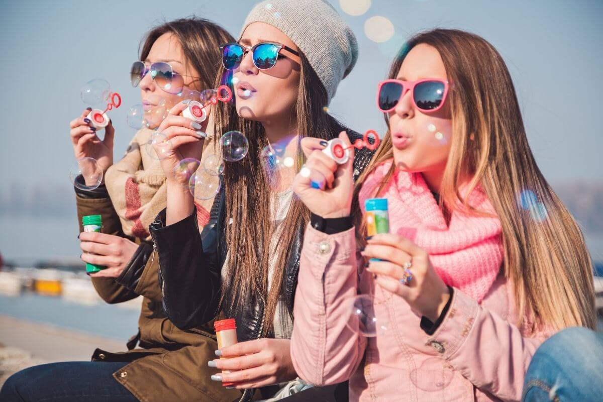 three young ladies enjoy positive social interactions as they blow bubbles together