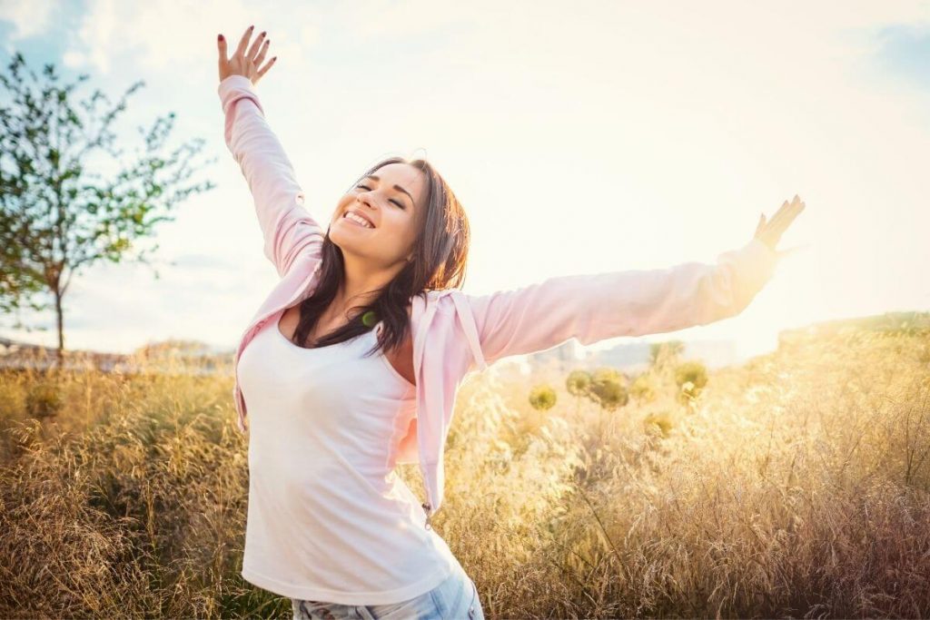 a happy woman stretches in the sunlight in a field