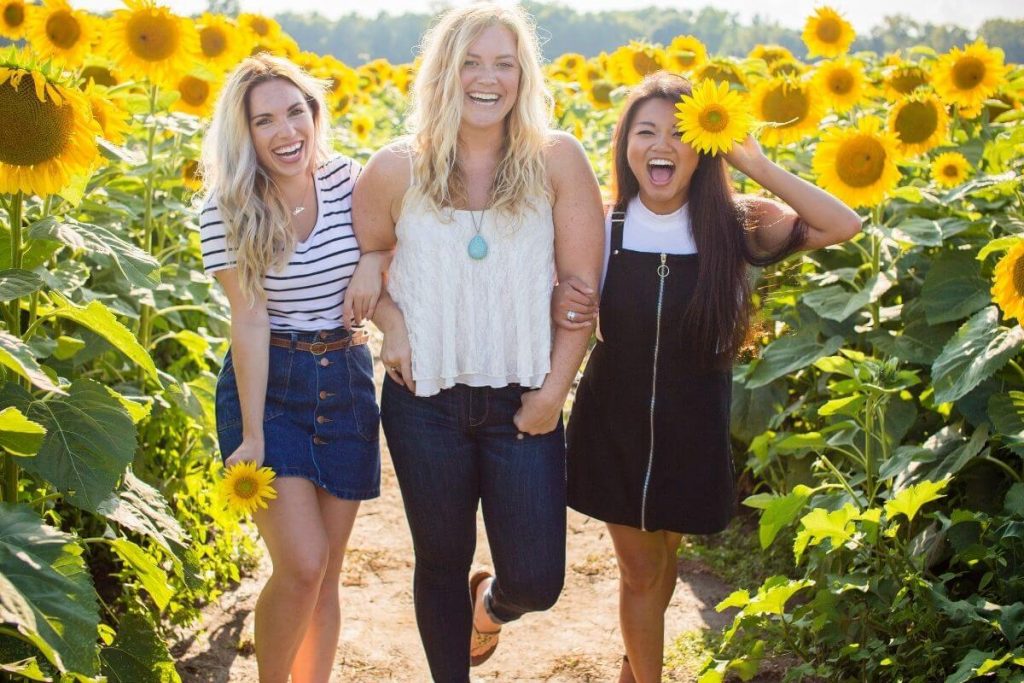 three happy women scroll through a sunflower field