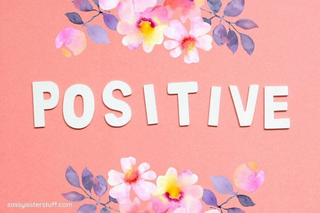 white letters spell positive on a peach background with flowers at the top and bottom of the image