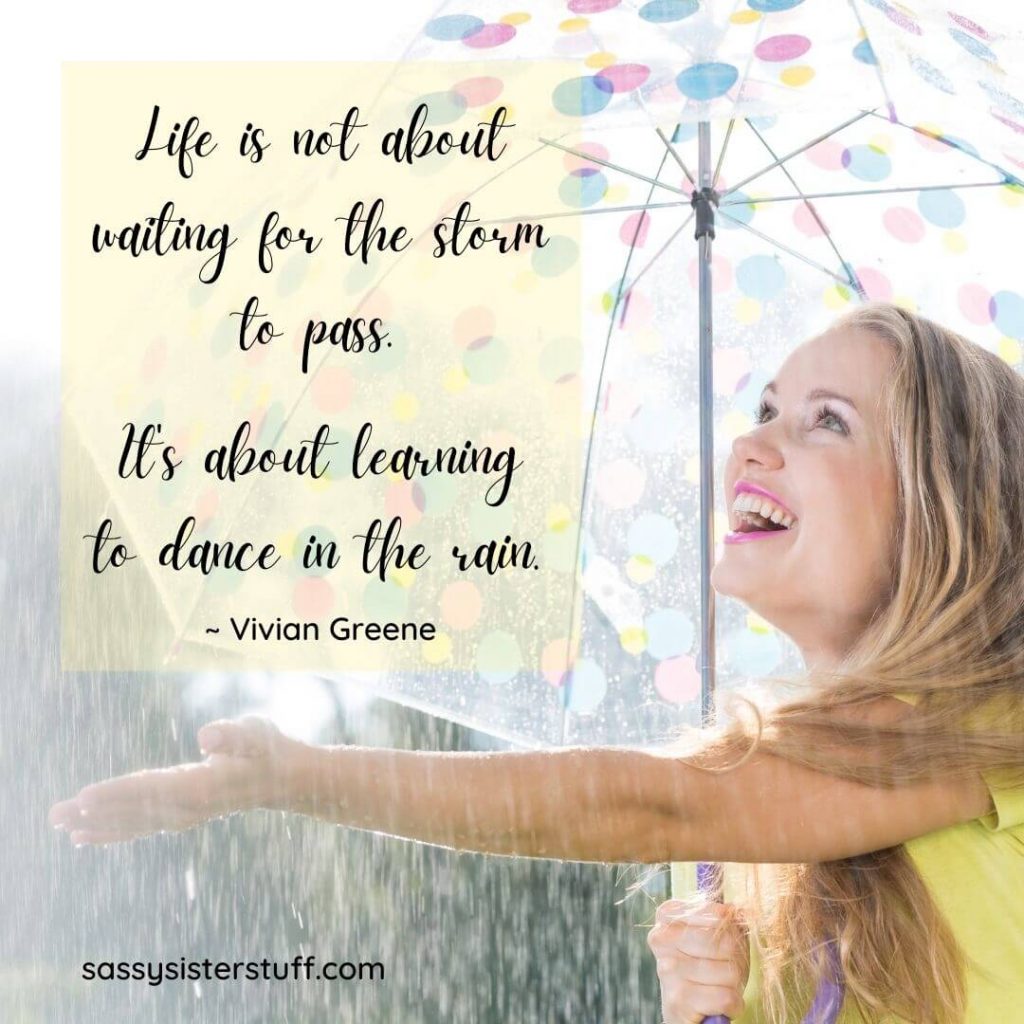 woman smiling under and umbrella reaching out smiling at the rain and a positivity quote