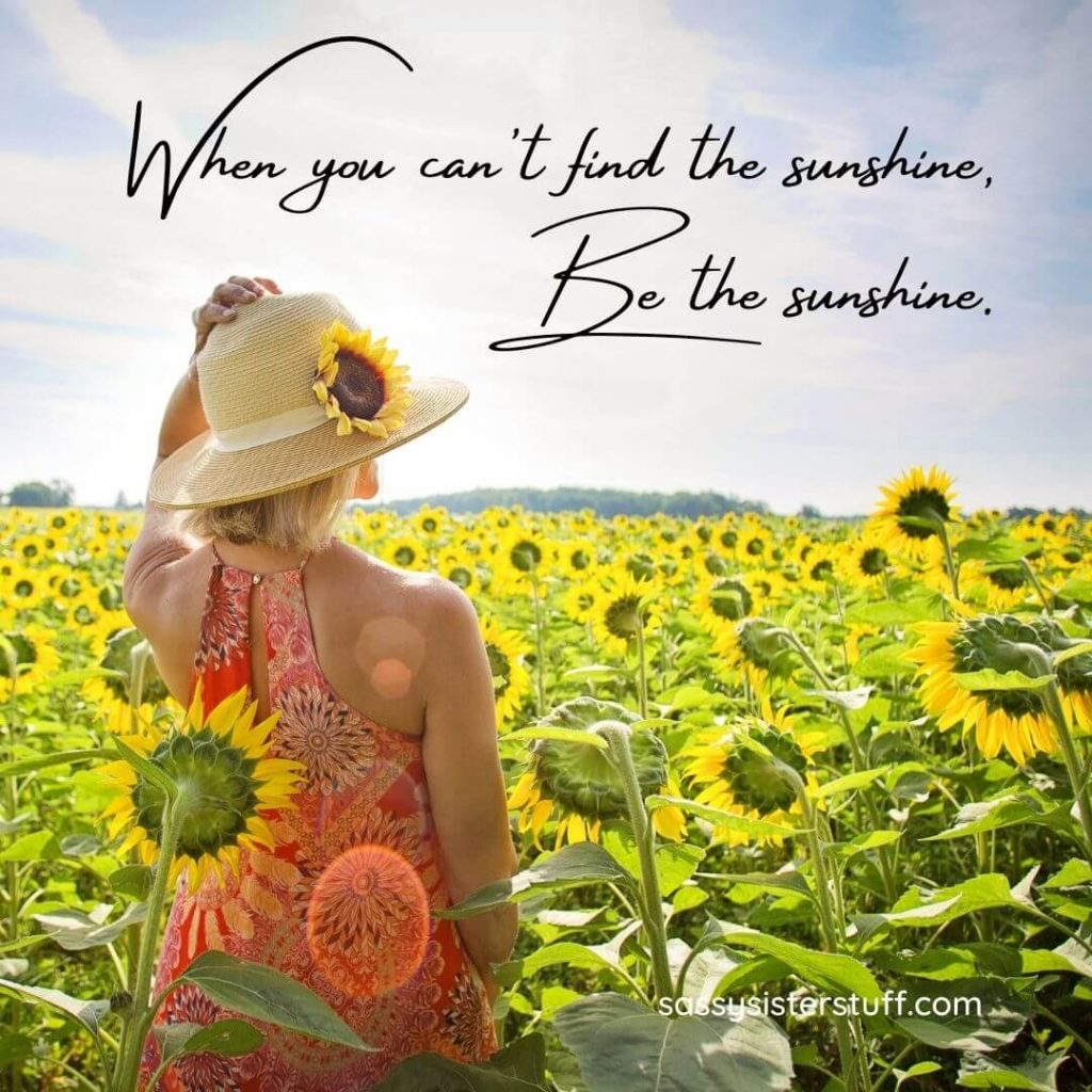 woman standing in a sunflower field with a positivity quote