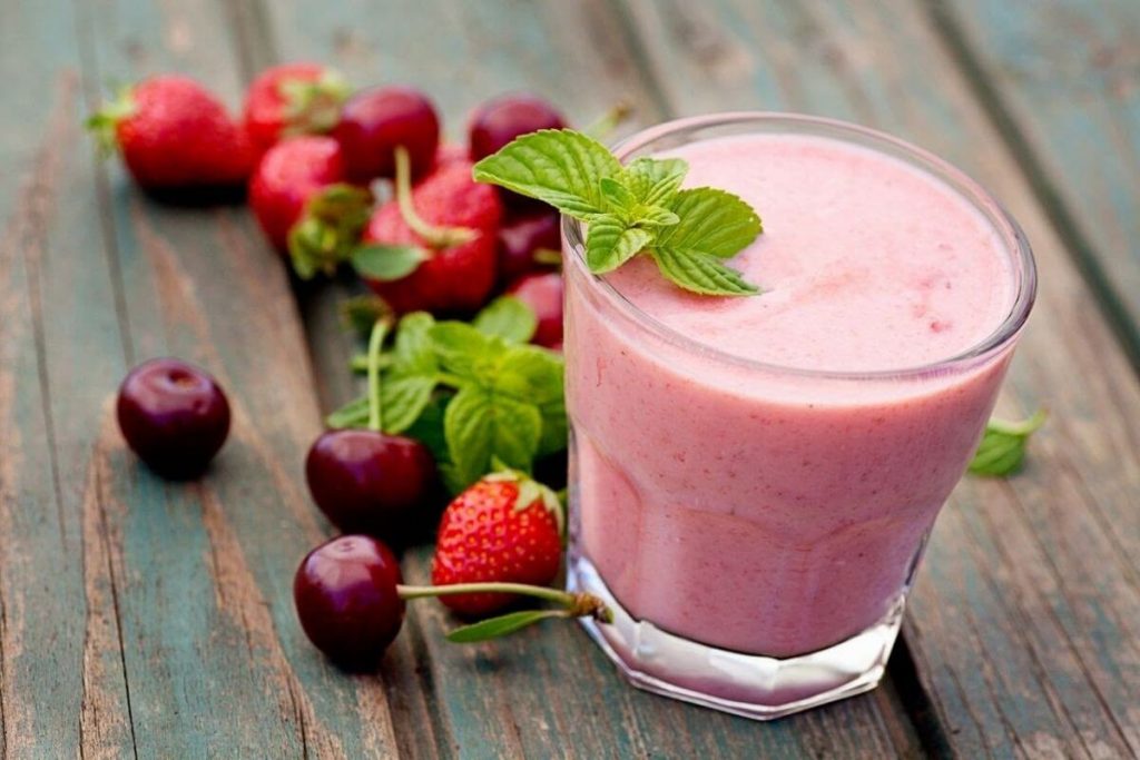 a berry smoothie with fresh berries laying next to the glass for a healthy breakfast