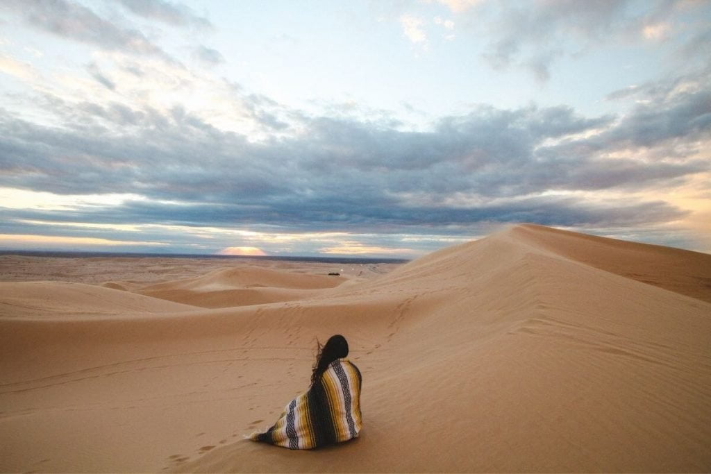 a traveler sits on a sand dune in the desert against a beautiful blue sky