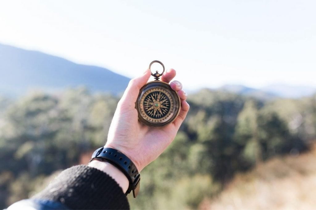 a traveler holds a compass in her hand looking out over mountains