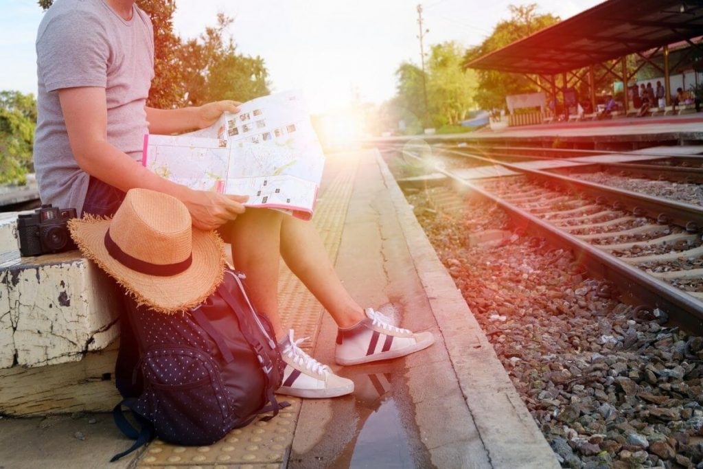 woman with travel bags sits at railroad staiong looking at a map waiting for a train