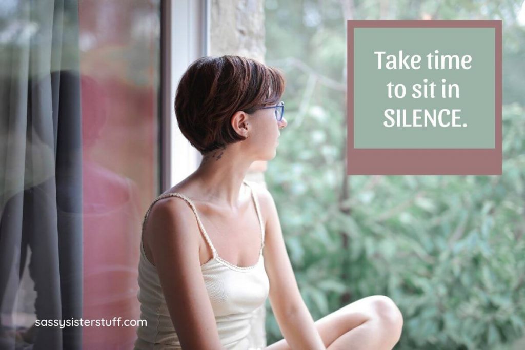 young woman sitting on a windowsill looking out the window in silence being mindful