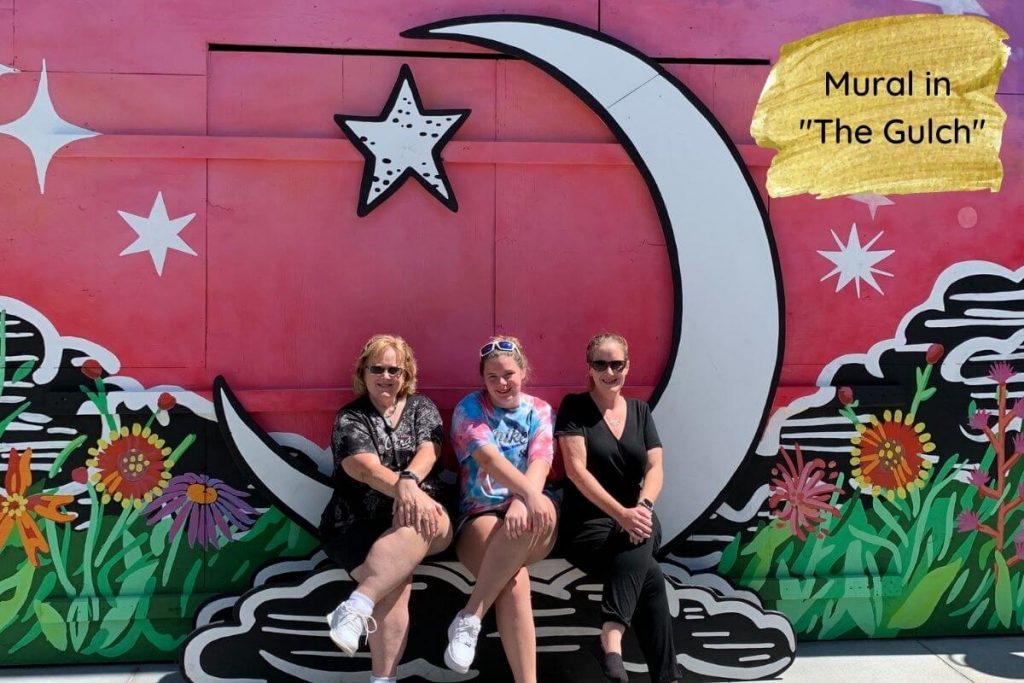 three happy women sit in front of a mural having family fun in Nashville