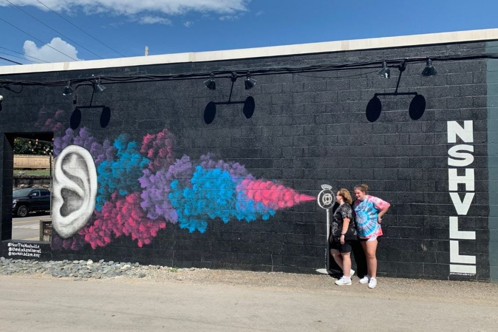 two women have fun taking a photo with a mural in Nashville