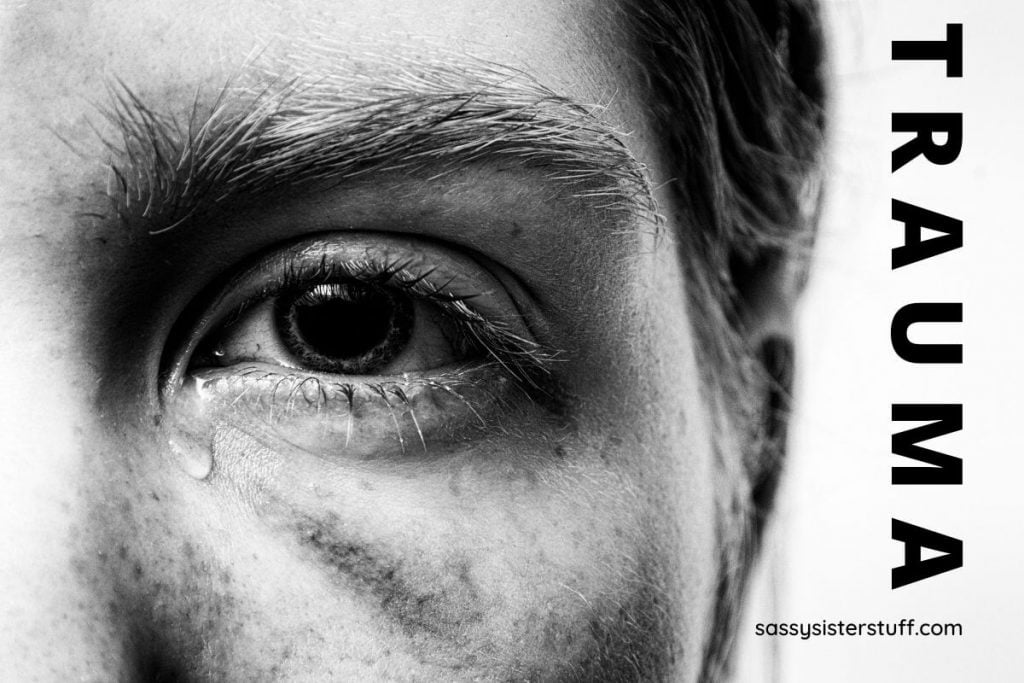 a closeup of a mans face with a tear drop coming from his eye and TRAUMA written along the edge of the image