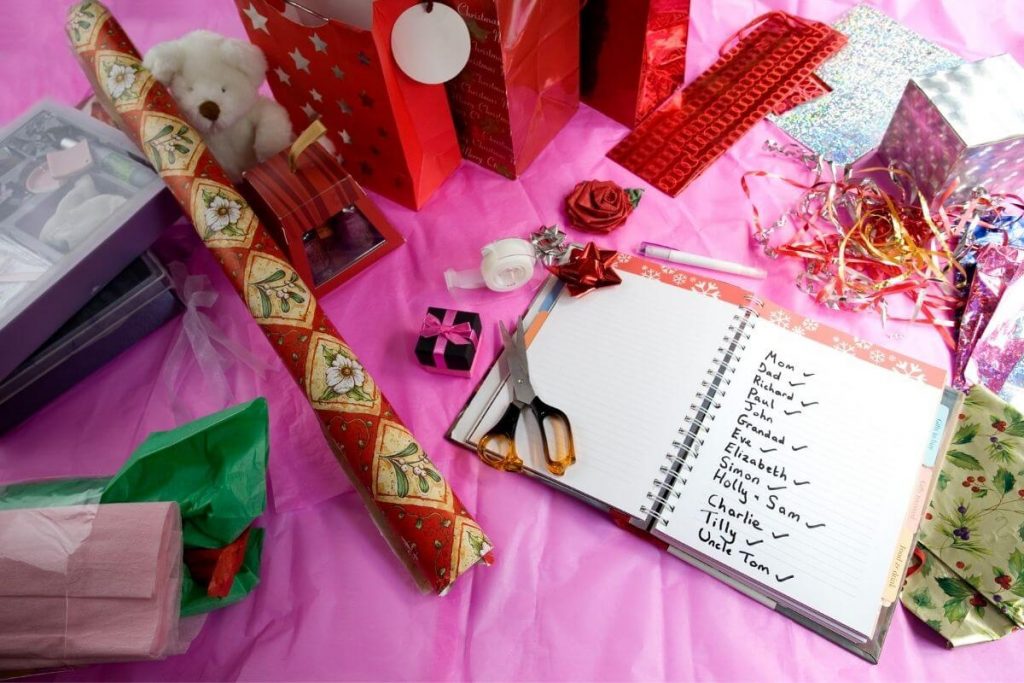 getting organized for the holidays with scissors a list wrapping paper gift bags labels tissue paper ribbon tape a pen all laying on a table