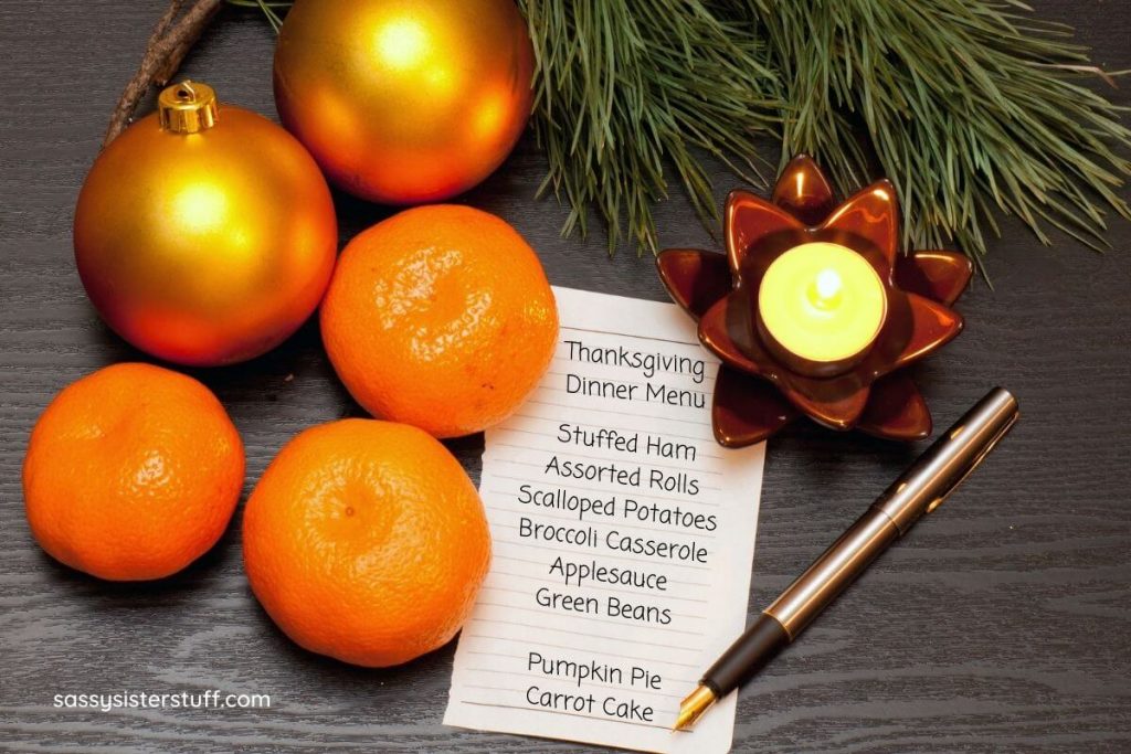 oranges a pine branch and a candle with a list that says Thanksgiving Dinner Menu