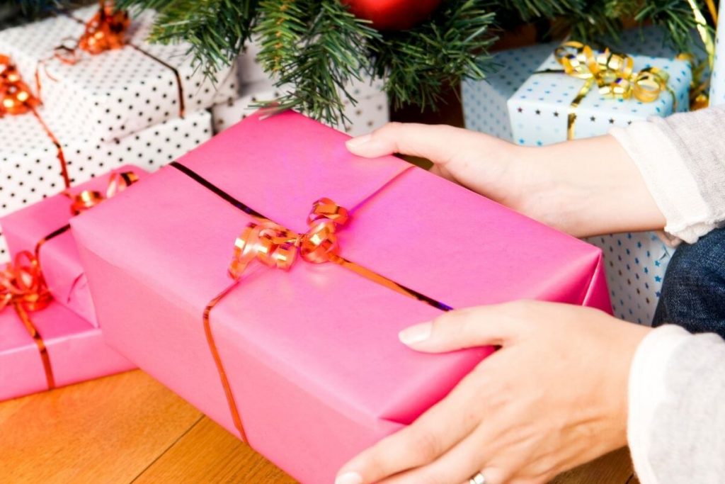 a woman is getting organized for the holidays by putting wrapped gifts under the tree