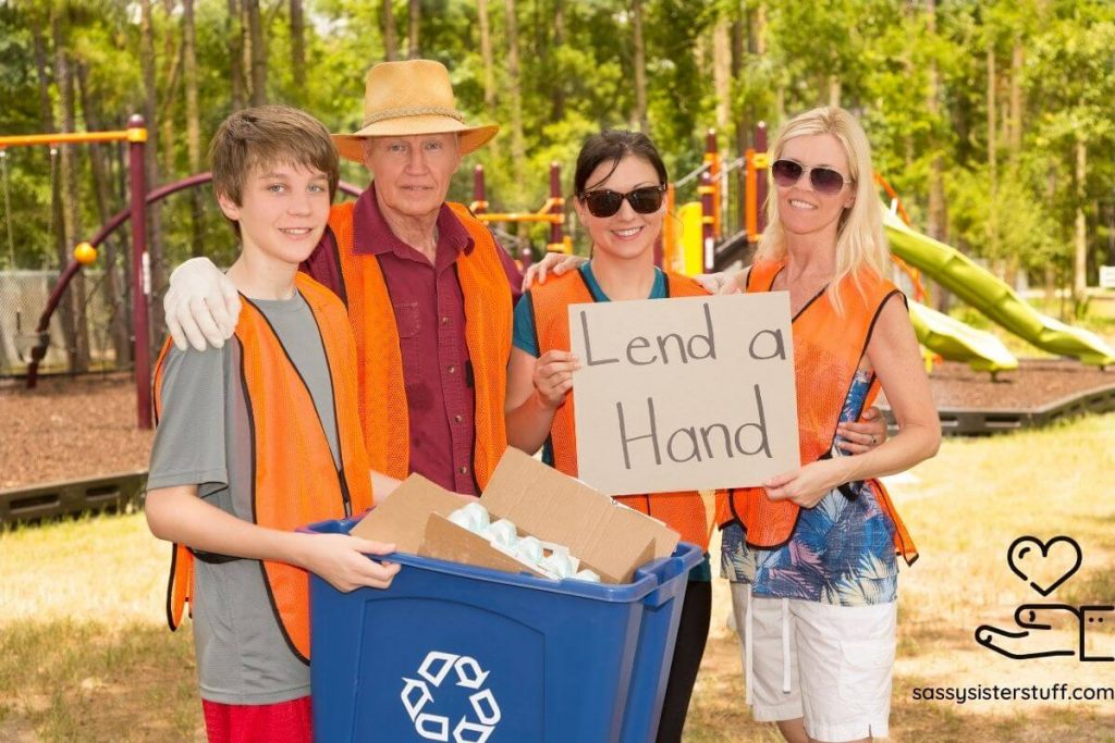 four people are cleaning a park with a recycle bin and holding a sign that says lend a hand