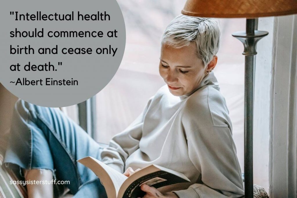 a casual woman sits in front of a window enjoying a book to show intellectual wellness tips to keep her brain healthy