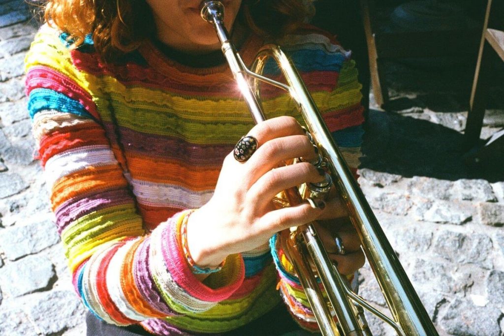 a woman in a colorful sweater plays the trumpet to show intellectual wellness tips involving learning to play an instrument