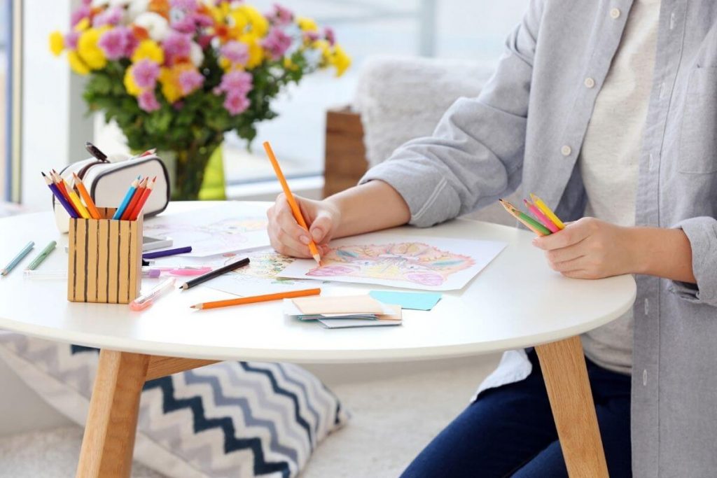 a woman colors on a table with flowers on self care Sunday